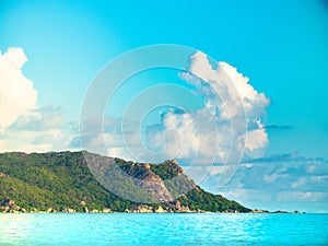 Blue waters of the Seychelles with green rocky outcropping and c