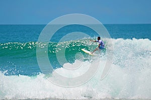 Blue wave of the ocean with splashes, in the background a surfer.