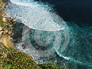 Blue wave of rip curl from the ocean splashes on yellow sand beach. Tropical sea danger.