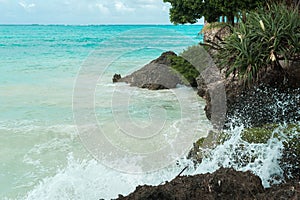 Blue waves break on the coastal rocks. Salt water spray in the light of the sun. Beach on Zanzibar island, Tanzania