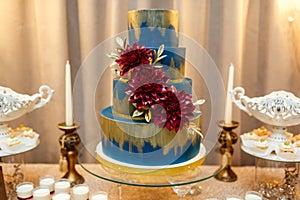 Blue wedding cake decorated by flowers standing of festive table with deserts, strawberry tartlet and cupcakes. Wedding