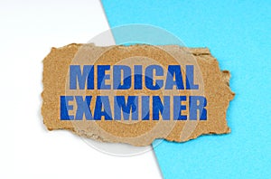 On a blue and white background lies a piece of cardboard with the inscription - MEDICAL EXAMINER