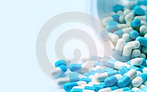 Blue and white capsules pill spilled out from white plastic bottle container. Global healthcare concept. Antibiotics drug