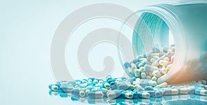 Blue and white capsules pill spilled out from white plastic bottle container. Global healthcare concept. Antibiotics drug photo