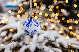 Blue white christmas ball on fir tree branch close up golden yellow light bokeh