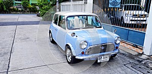 Blue/White classic Mini cooper parked on the street in front of home`s entrance door with sunlight