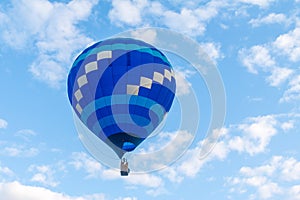 A blue and white hot air balloon floats against a blue and white sky