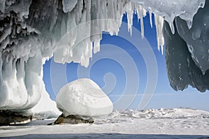 Blue white ice cave with icicle stalactites, blue sky and stone covered ice