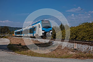Blue and white modern passenger train is closing to a station on local branch line. Sunny day, train travelling through sun photo