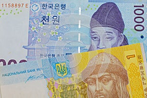 A blue and white one thousand won bill from Korea paired with a blue, white and yellow one hyrvnia bank note from Ukraine.