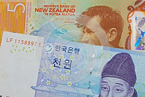 A blue and white one thousand won bill from Korea paired with a orange, plastic five dollar bill from New Zealand.