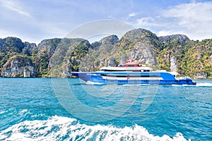 Blue with white and red accents pleasure speed boat. Sailing on the sea against a tropical mountain island. Side view. Motor track