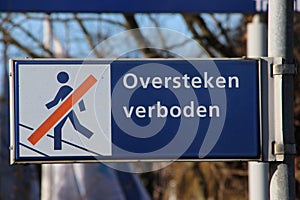 Blue and white sign with dutch language text `oversteken verboden` which means that trespassing the rails is not allowed
