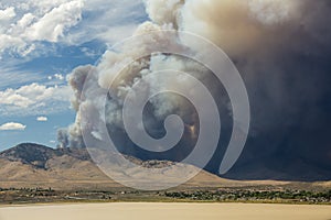 Blue and white sky puffy cumulonimbus clouds and smoke from a large wildfire in the desert muddy lake in foreground