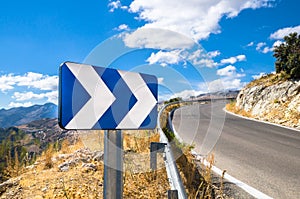 Blue white street sign showing directions next to a road with a scenic background