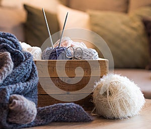 Blue and white woolen balls in a wooden box with a blue knitted scarf and knitting needles