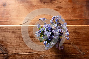 Blue wildflowers in a glass cup on a wooden background. Forget me nots.