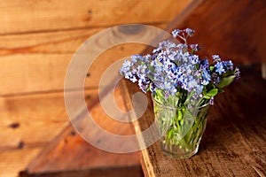 Blue wildflowers in a glass cup on a wooden background. Forget me nots.