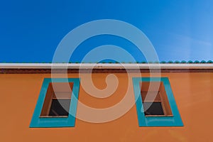 blue window frames on orange colored house facade with green tiled roof