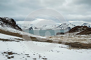 Blue winter lake and snow mountains. Dirt road to the lake is covered with snow