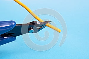 Blue wire cutter cuts yellow wire on blue background