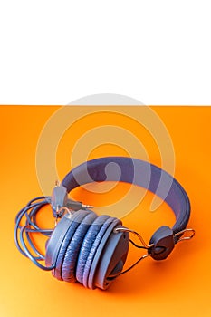 Blue wired headphones with black 3.5 jack on orange background