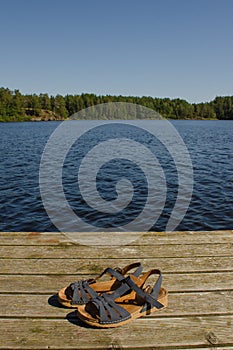 Blue women`s sandals on a wooden pier in summer against the background of water and sky. Travel hiking concept, vertical photo