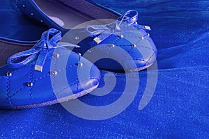 Blue women shoes isolated on blue mesh fabric. A pair of dark blue women`s flat shoes, copy space, boutique women`s