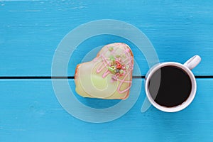 Blue wood background with cup of black coffee and heart shape donut. Top view