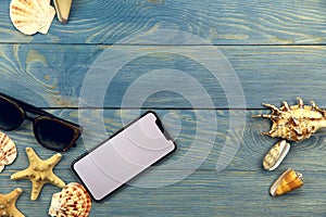 On the blue wooden background on the left are sunglasses, a telephone and different shells, on the right are three seashells.