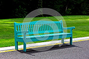 A blue wooden bench lit by sunlight stands on an asphalt road.