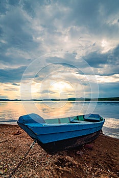 Blue wooden boat moored on the shore of lake under cloudy sky at sunset