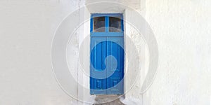 Blue wooden door on empty white wall background. Greek island house front view