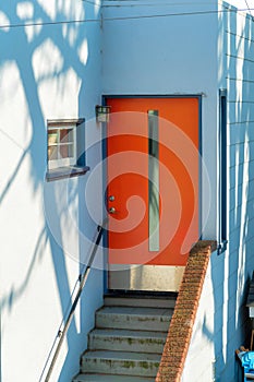 Blue wooden house facade with red door and brick handrail on front yard stairs in shade late afternoon