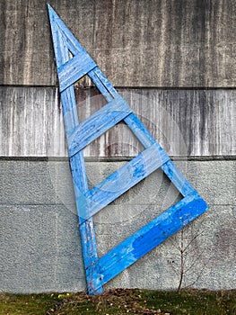 Blue wooden outdoor structure, shape as an arrow on dirty rough concrete wall.