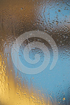 Blue-yellow background of wet glass with raindrops, splashes and