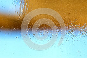 Blue-yellow background of wet glass with raindrops, splashes and