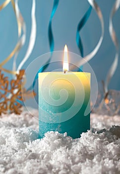 Blue and yellow burning christmas candle in the snow agains blue background