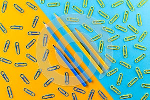 Blue and yellow colored pencils and paperclips in the blue and yellow background