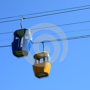 Blue and yellow passenger cable way cabins in the clear sky