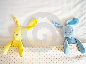 Blue and yellow rabbit doll laying on white bed under cream blanket pink polka dot pattern