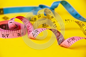 Blue, yellow and red measuring tape on yellow background. Copy space and weight loss concept.