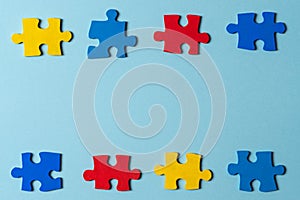 Blue, yellow, red pieces of puzzle on light blue frame background. World autism awareness day concept. Top view, copy