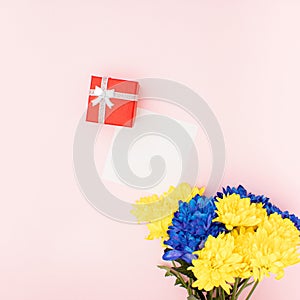 Blue and yellow spring flowers bouquet, red gift box and note card on a pastel pink background. Minimal romantic flat lay