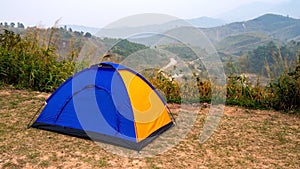 Blue and Yellow tourist camping tent in recreation area among meadow in mountain forest