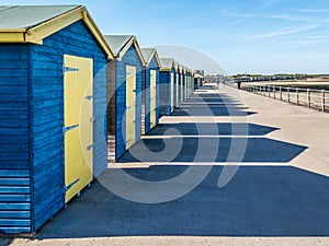 Blue and yellow wooden beach huts casting long shadows