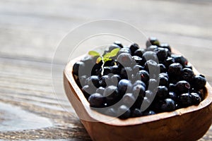 Blueberries Bilberries with green leaf into a bowl on brown wooden background, many fresh dark blue berries