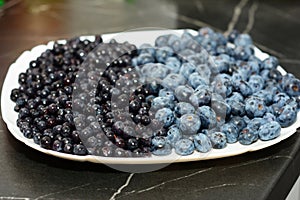Blueberries and bilberries on the white plate. Ripe bilberries are smaller and darker than blueberries