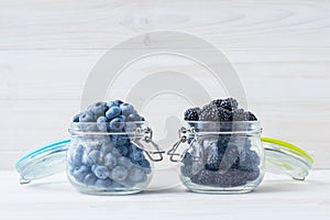 Blueberries and blackberries in a bowl on a white wooden table. Berries in a glass jug. Vegetarian food concept. Copy space, empty