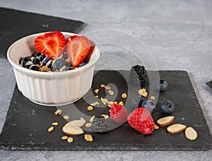 Blueberries, blackberries, raspberries and strawberries with yogurt sauce, granola and sliced almonds served in a white ramekin